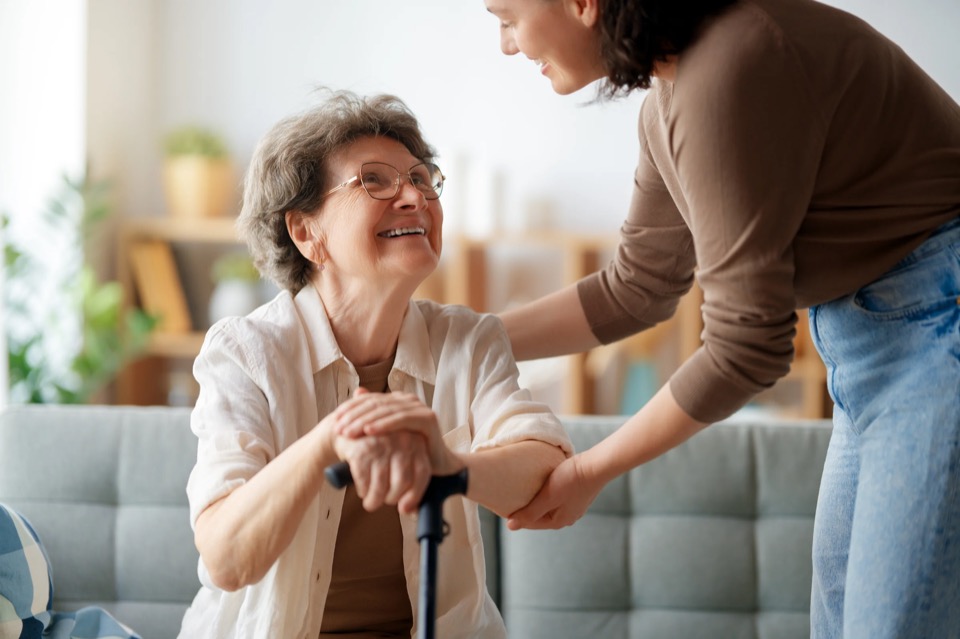 Seniorin mit Gehstock verbringt gemeinsam mit ihrer Pflegekraft Zeit.